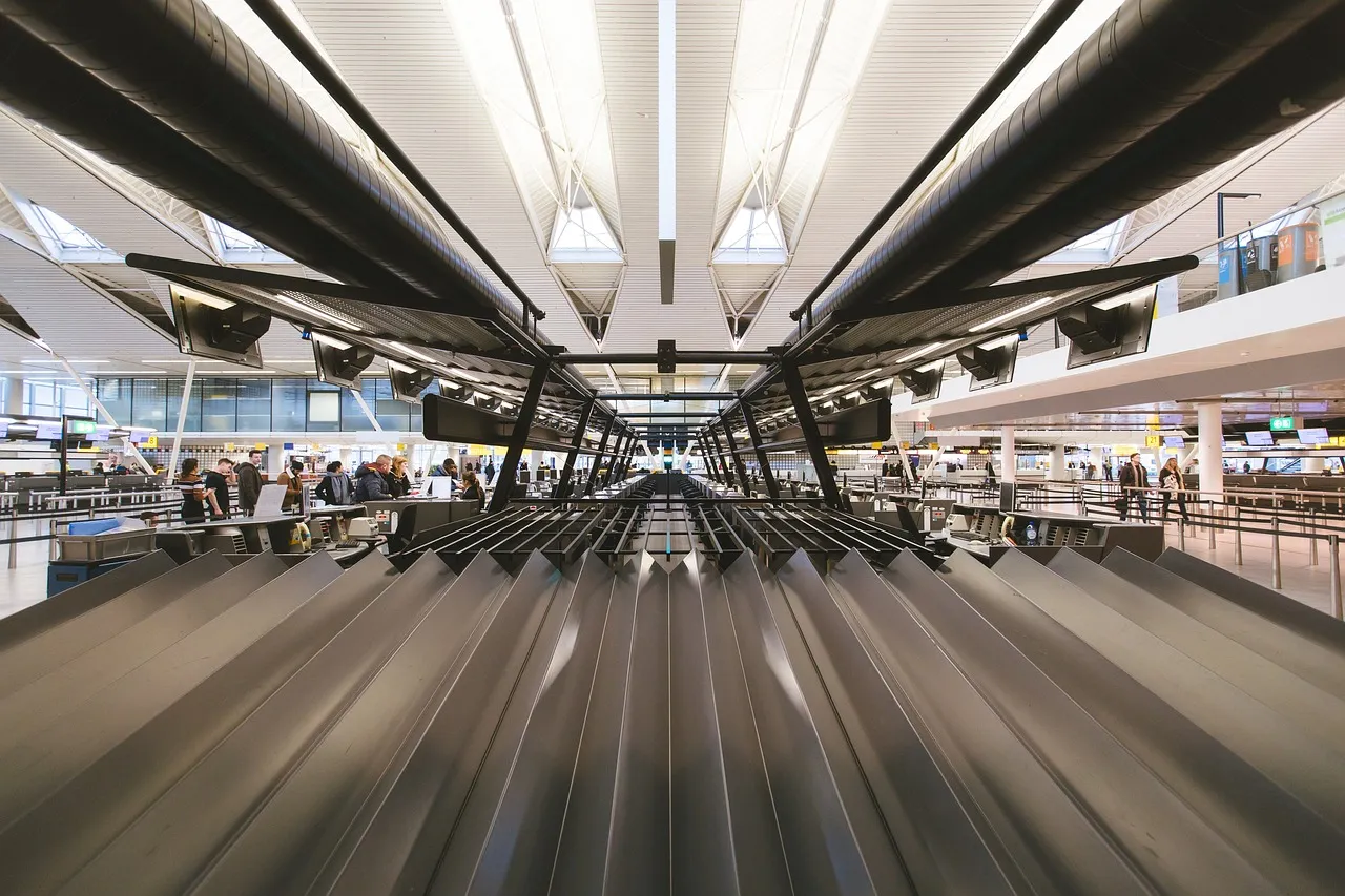 Baggage belts at a row of check-in desks in a bright airport hall with a white roof