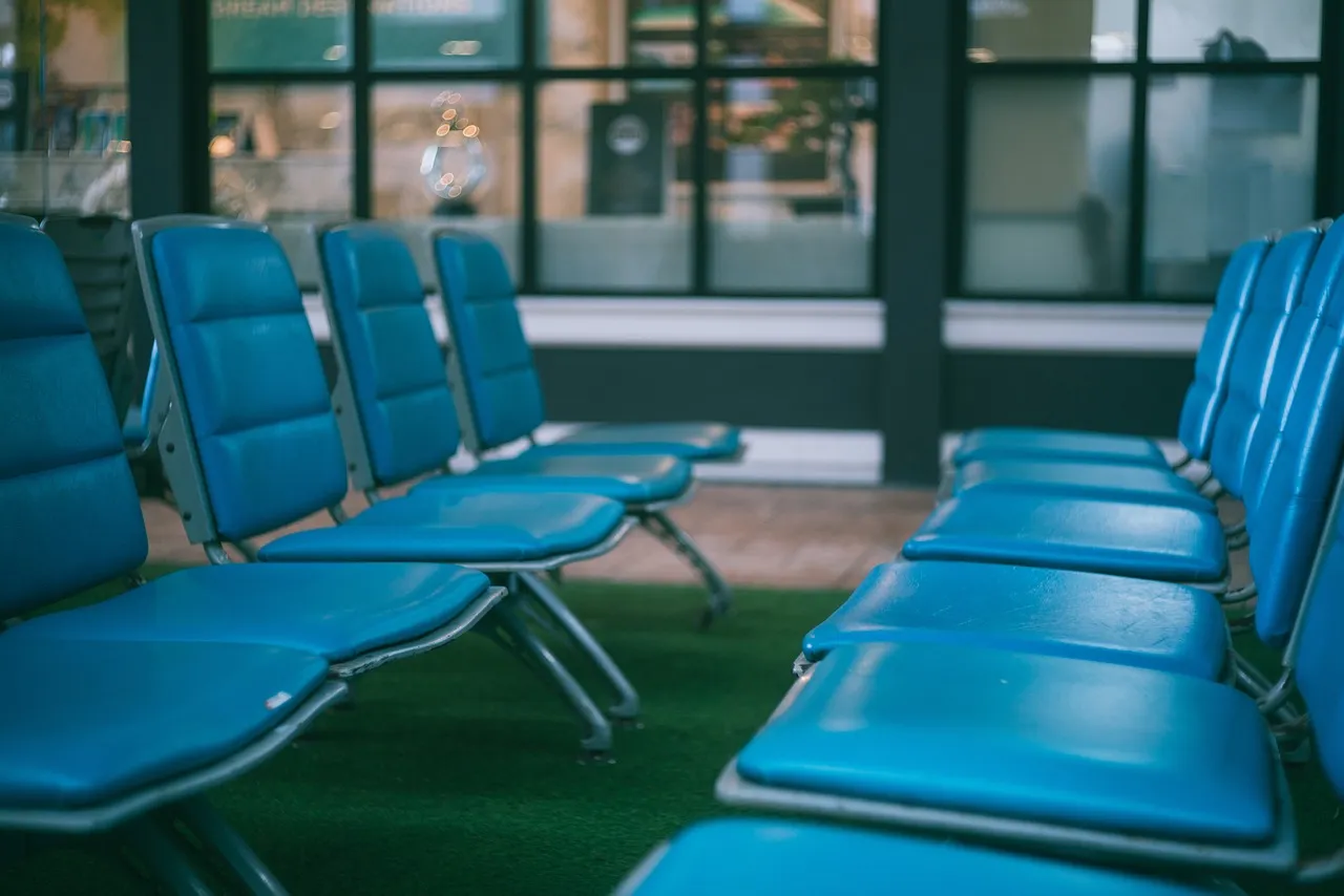 Rows of empty blue seats in an airport departure lounge, with large windows behind