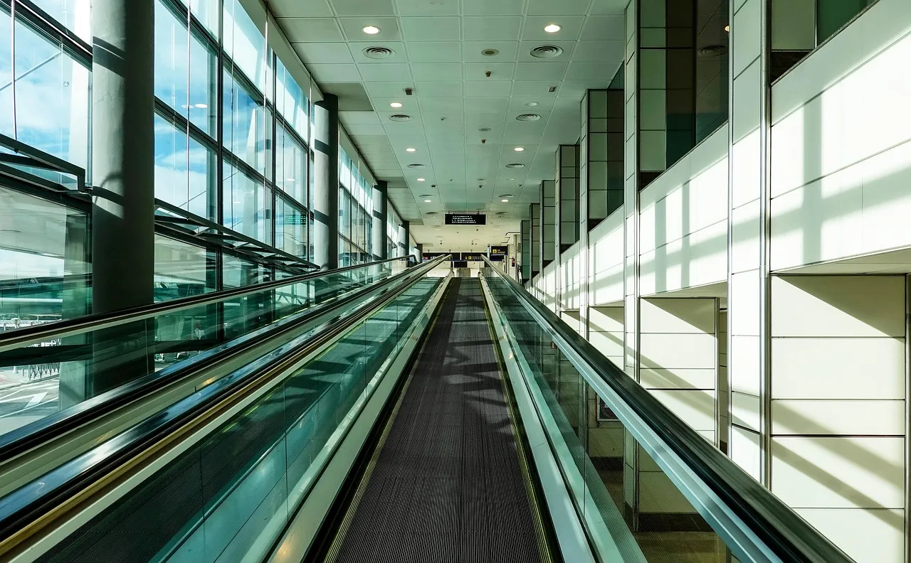 A long moving walkway in a bright airport terminal with tall windows on one side