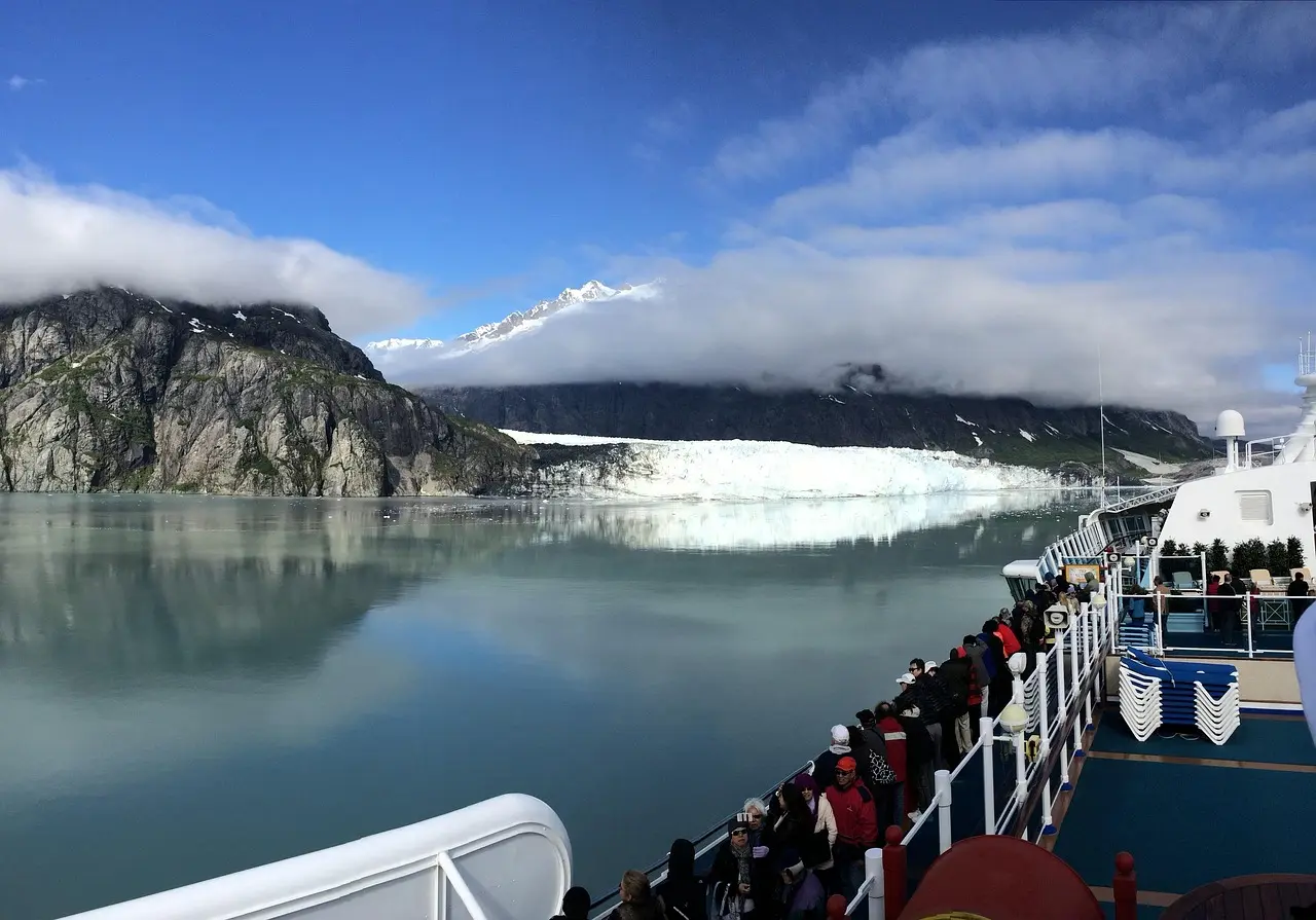 Passengers on the deck of a cruise ship looking out at a glacier and mountains in Alaska