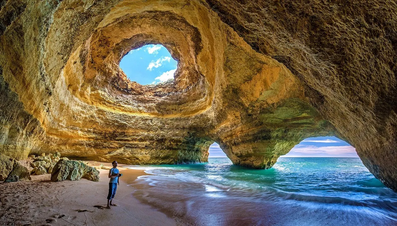 Sunlight pouring through the round opening in the roof of Benagil sea cave onto a small sandy beach