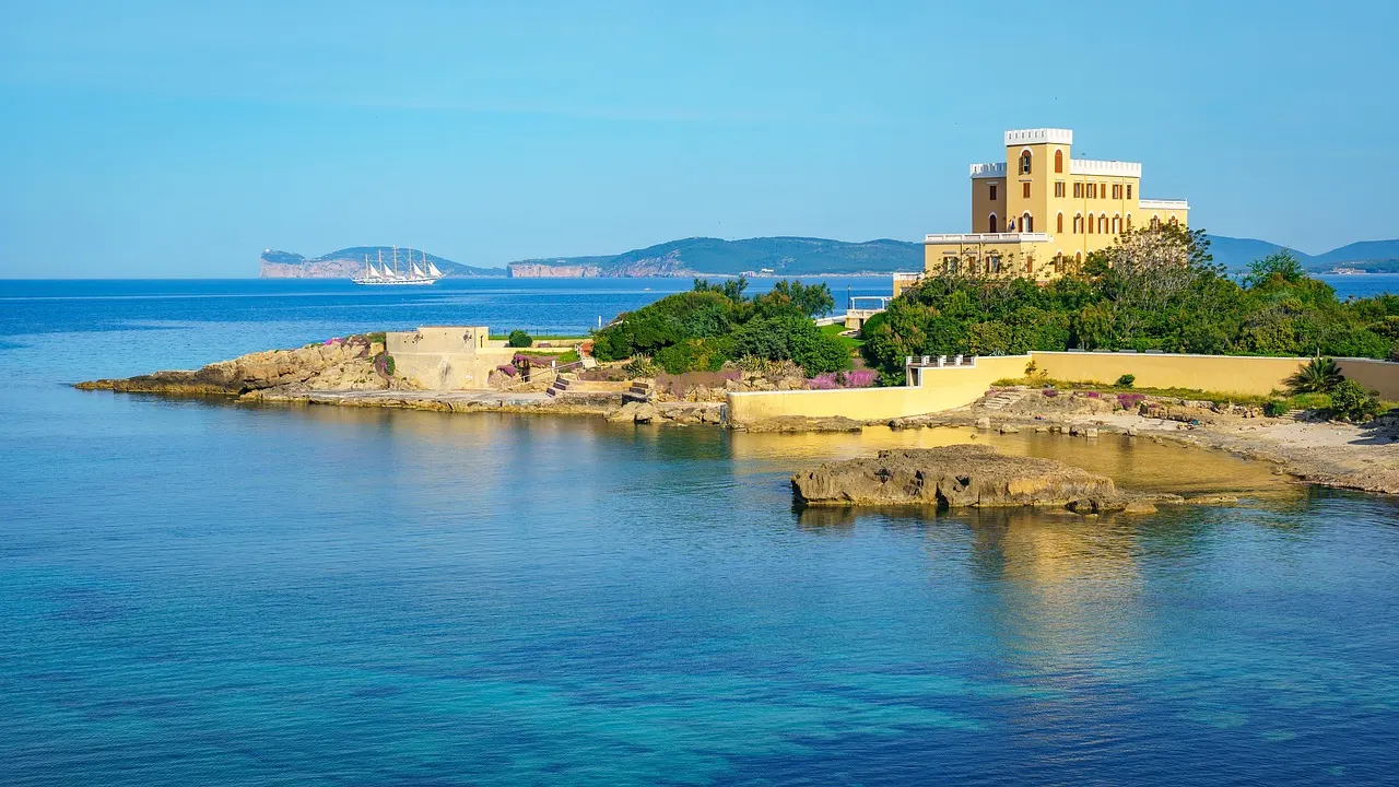 Villa Las Tronas on a rocky point above clear turquoise water in Alghero, with the headland of Capo Caccia in the distance