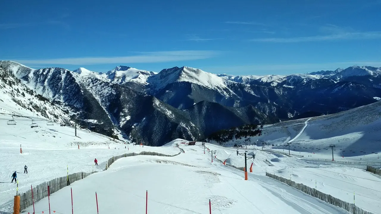 Skiers on groomed pistes at Arinsal in Andorra, with snowy Pyrenees peaks under a blue sky