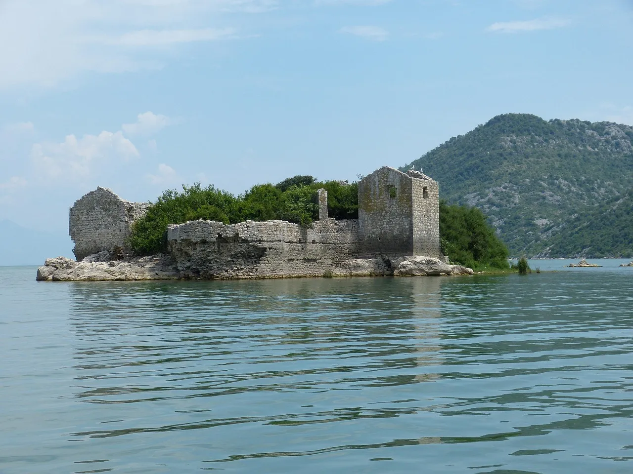 Lake Skadar in Montenegro, with an old stone fortress on a small island and mountains behind, near the end of the Belgrade to Bar railway
