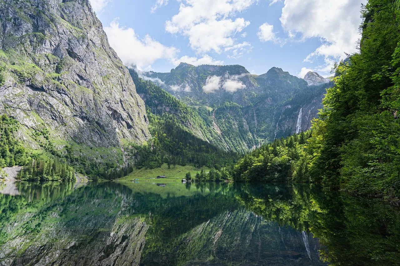The Obersee lake near the Königssee in Berchtesgaden, reflecting green forest and steep rock walls with a waterfall