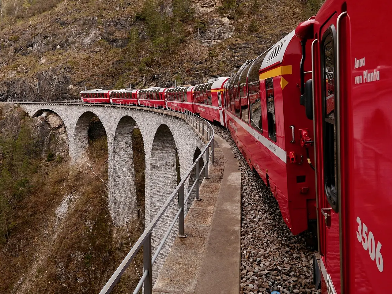 A red Bernina Express train curving onto a tall stone viaduct over a deep gorge, seen from a window