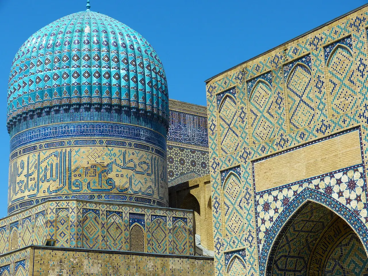 The ribbed turquoise dome and tiled walls of the Bibi-Khanym Mosque in Samarkand under a clear blue sky