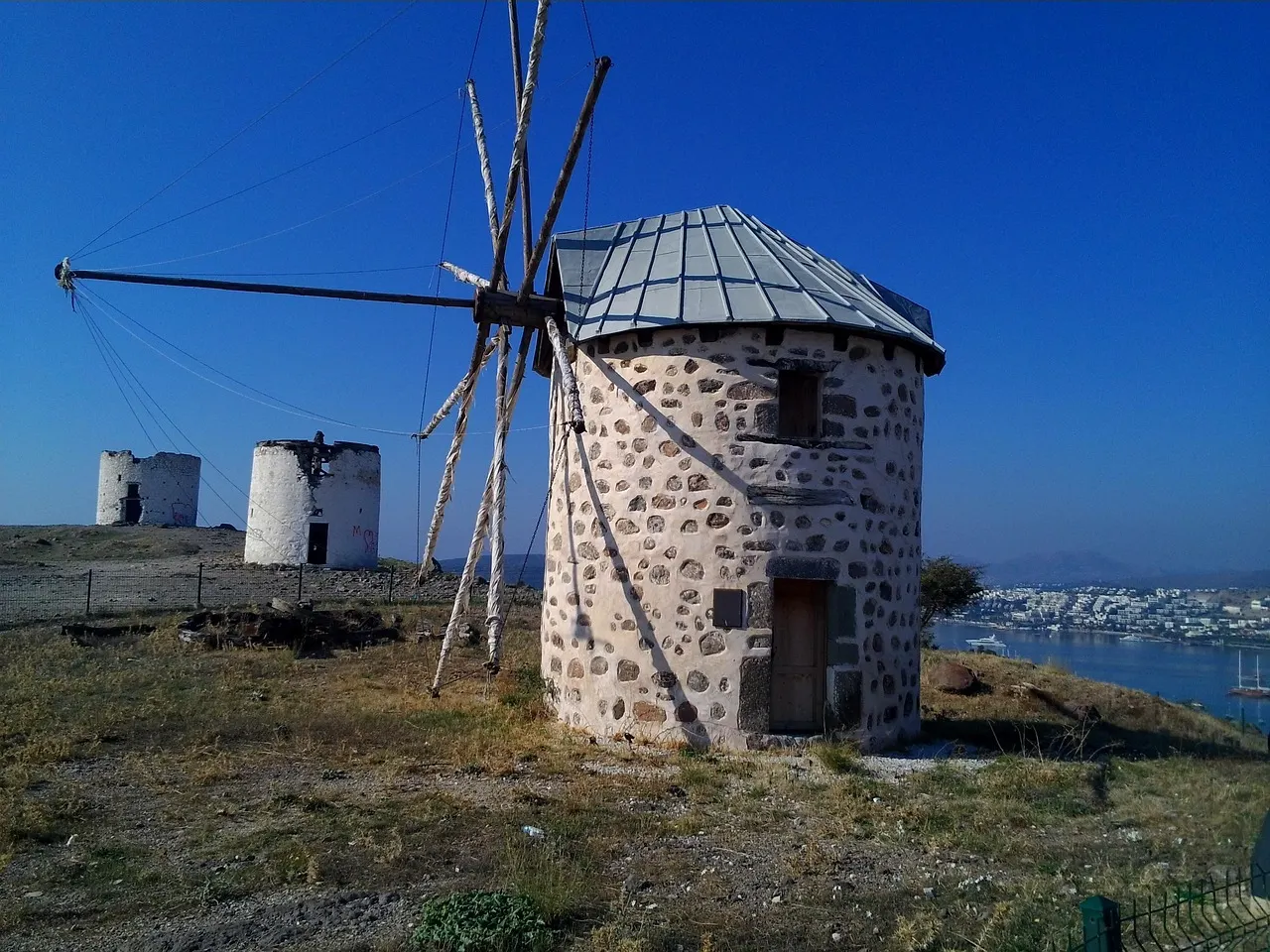 A stone windmill on a hill above Bodrum, with more windmills and the sea behind under a blue sky