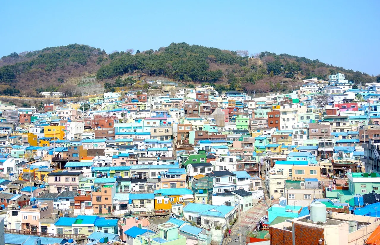 The brightly painted houses of Gamcheon Culture Village climbing a hillside in Busan, with green hills behind