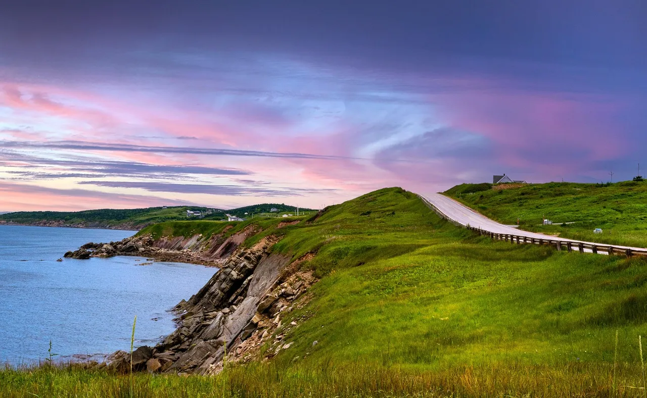 The Cabot Trail curving over green clifftops above the sea on Cape Breton Island at sunset