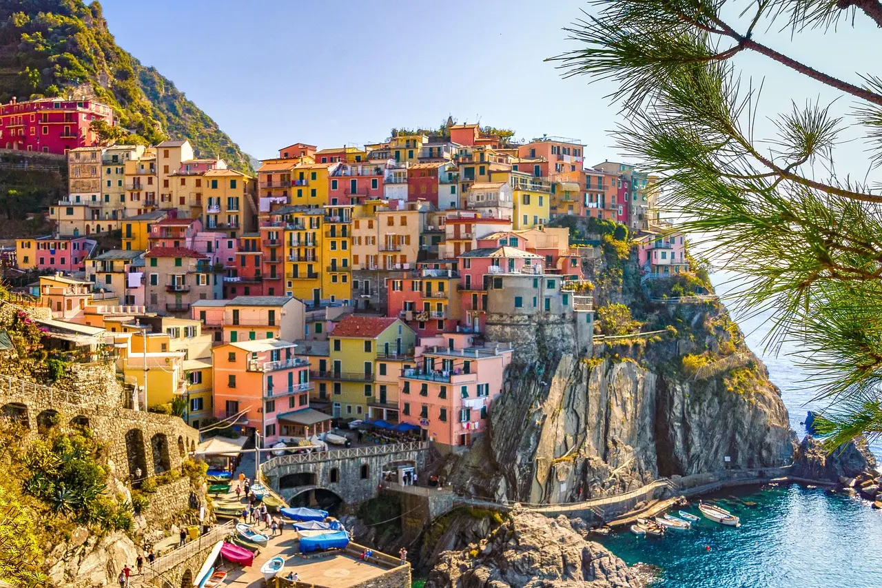 Colourful houses stacked on a cliff above the sea at Manarola, framed by pine branches