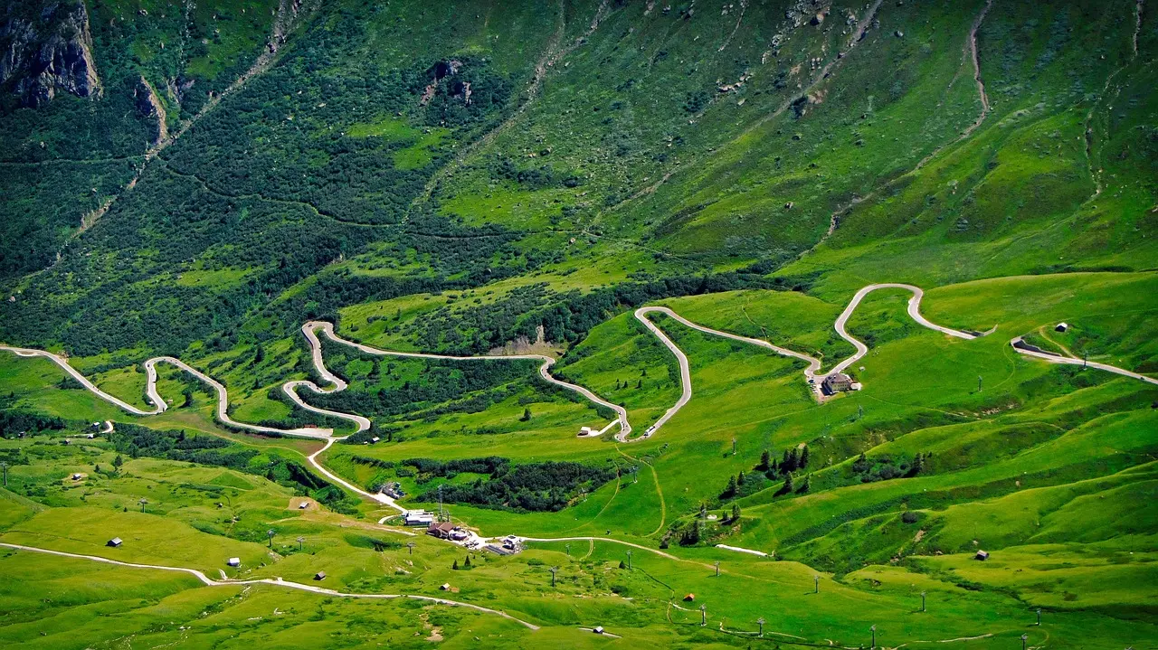 A mountain pass road zigzagging through bright green alpine meadows in the Dolomites