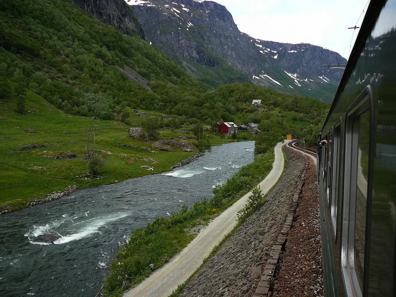 A view from the Flåm Railway train window of a rushing river and green valley below steep mountains