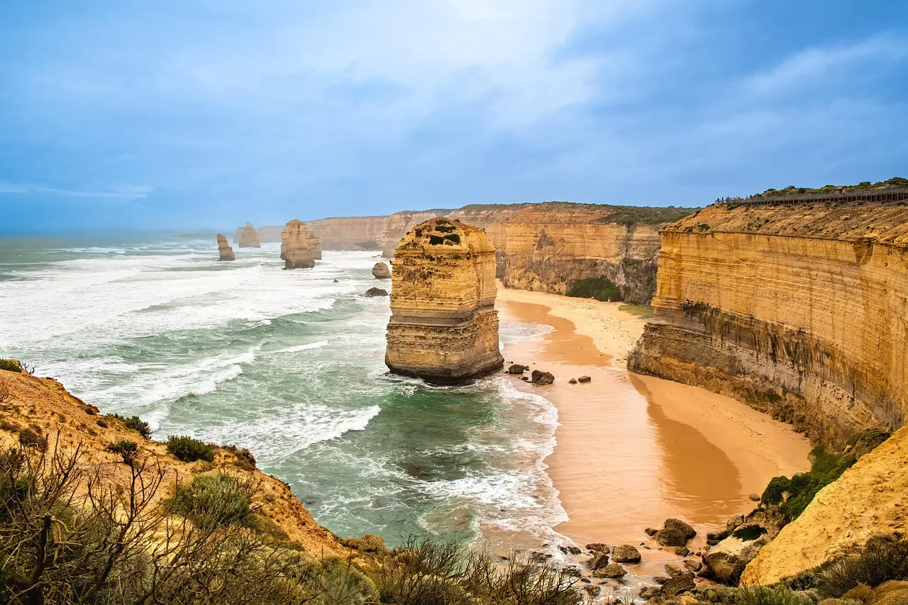 Limestone stacks of the Twelve Apostles standing in the surf below golden cliffs and a sandy beach