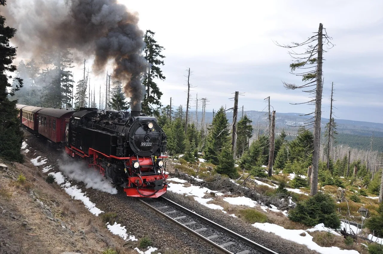 A Harz narrow-gauge steam train climbing through snowy forest towards the Brocken, with clouds of smoke above