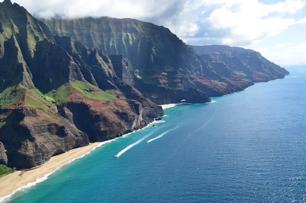 A boat sailing along the steep, green, folded cliffs of the Na Pali Coast on Kauai