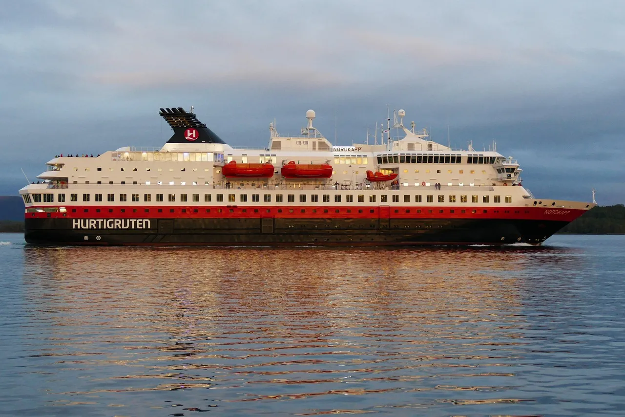 A red, black and white Hurtigruten ship sailing along the calm Norwegian coast under a pale sky