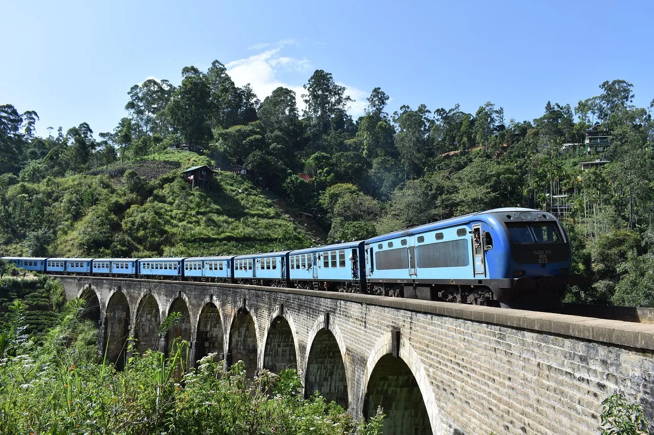 A blue Sri Lankan train crossing the stone Nine Arch Bridge near Ella, surrounded by thick green forest