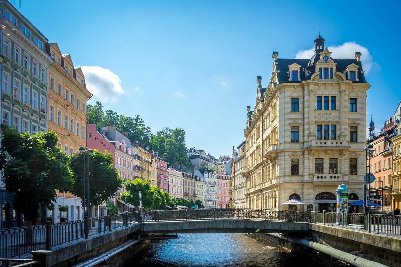 Grand pastel-coloured spa buildings beside the river Teplá in Karlovy Vary, under a blue sky