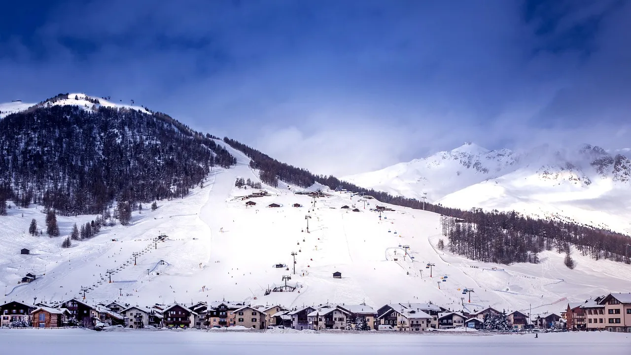 Snow-covered slopes and ski runs rising above the long village of Livigno in the Italian Alps under a cloudy blue sky