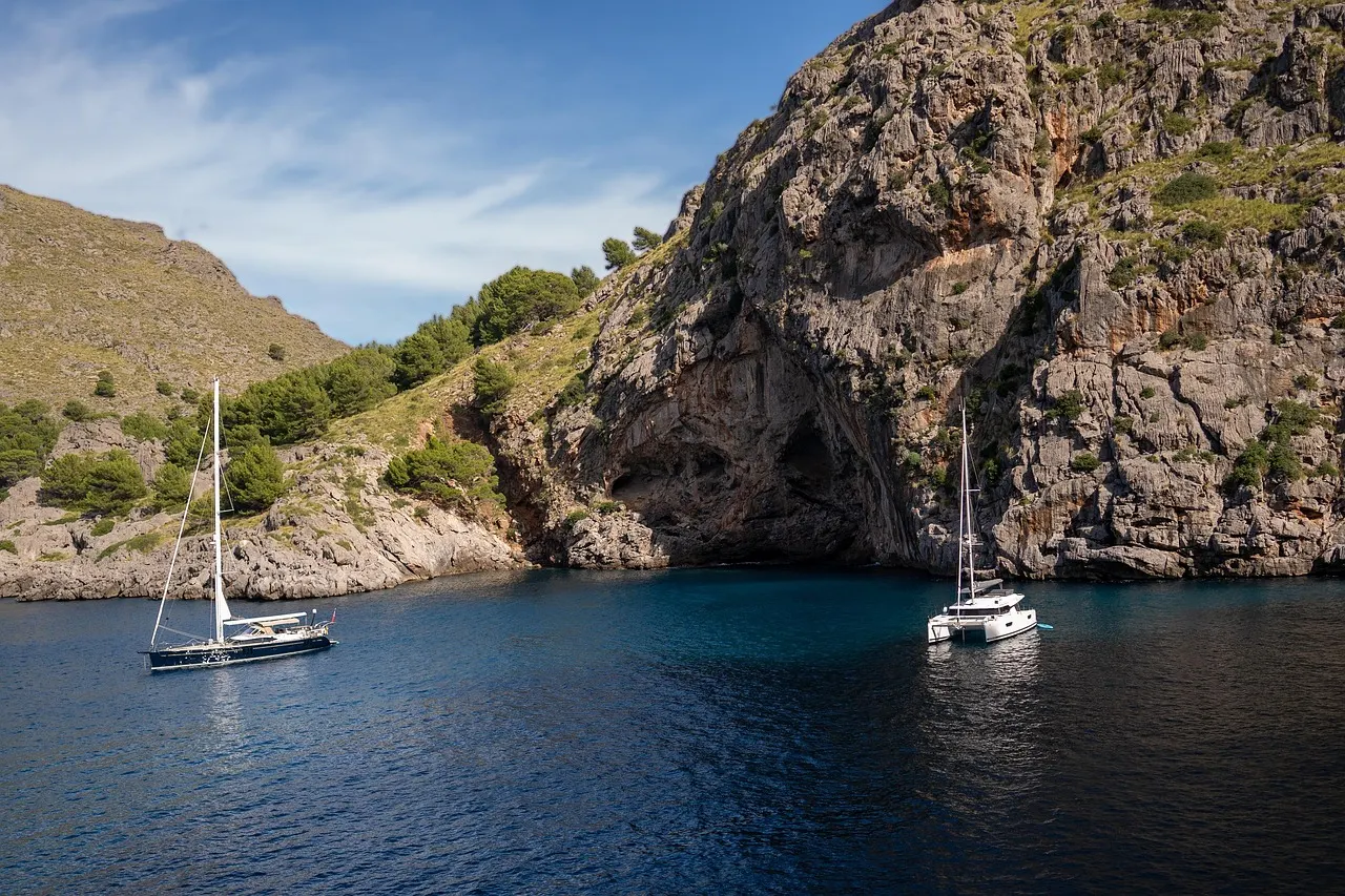 Sailing boats moored in a deep blue cove below rocky, pine-covered cliffs on Mallorca's coast