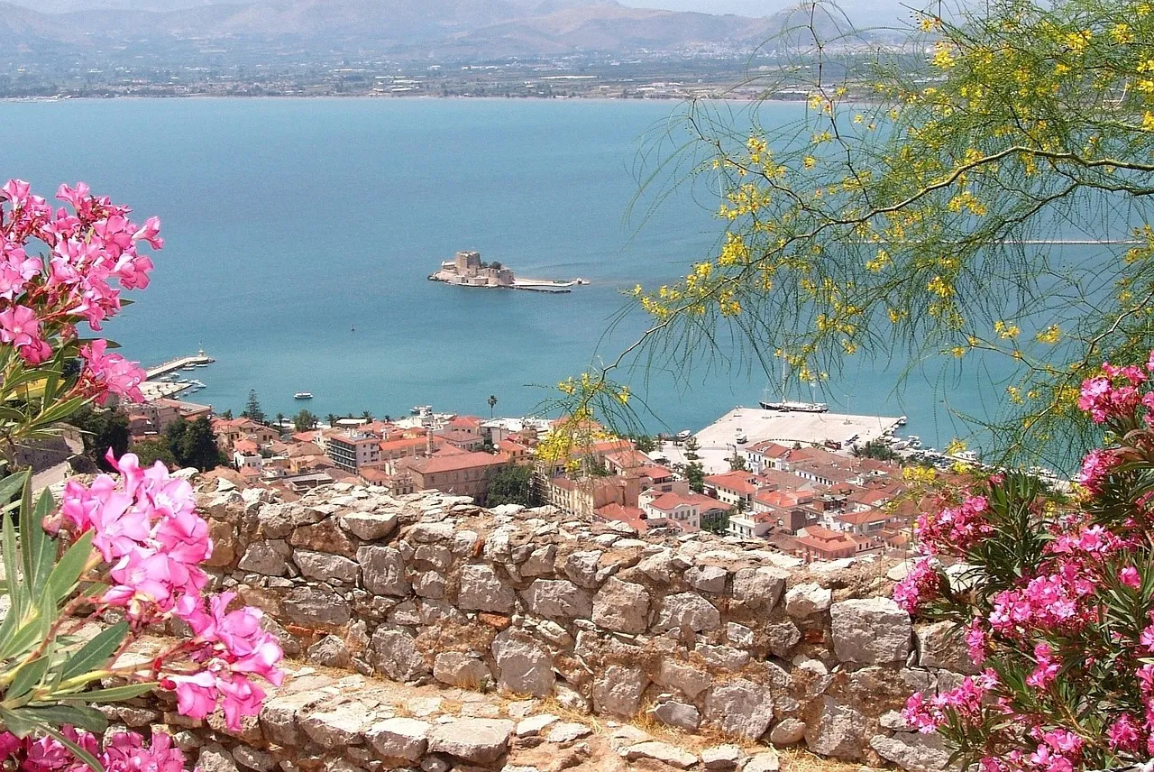 View over the tiled roofs of Nafplio's old town to the little Bourtzi sea castle in the bay, framed by pink oleander and an old stone wall