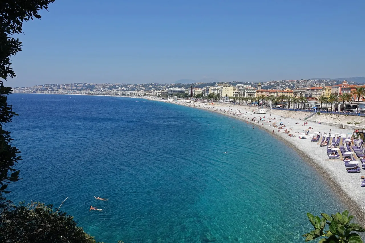 The Promenade des Anglais curving around the blue Baie des Anges in Nice, with a pebble beach below