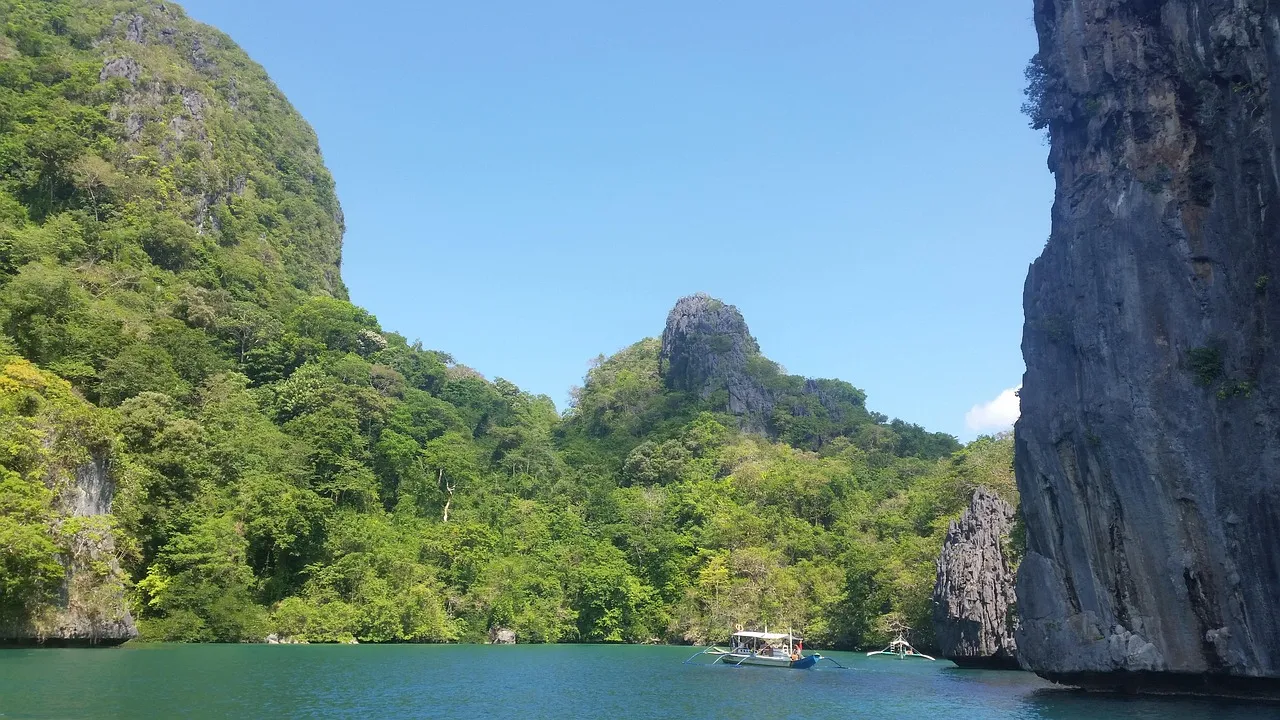 Tall limestone cliffs covered in jungle rising from a calm turquoise lagoon near El Nido, Palawan