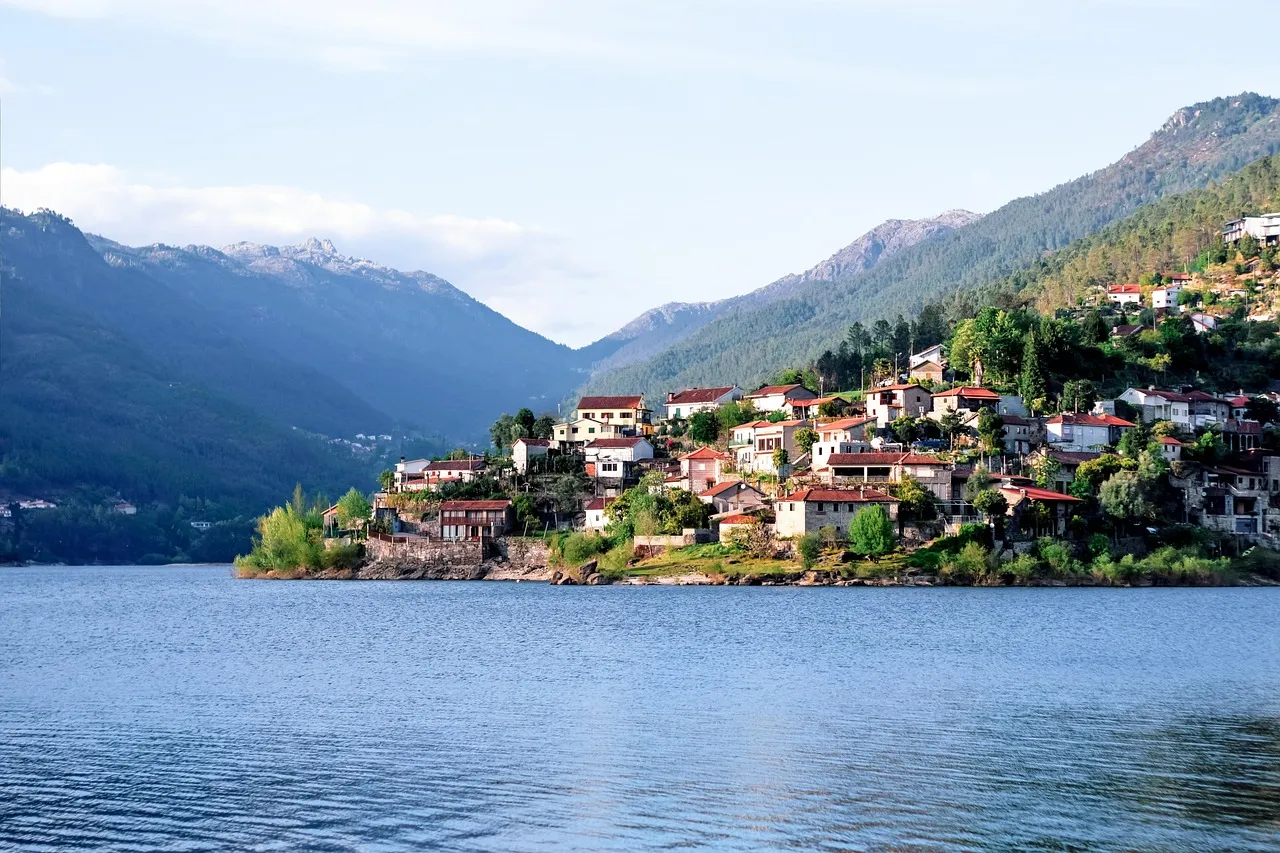 A village of white houses on a green hillside above a reservoir in the Gerês mountains, with peaks behind