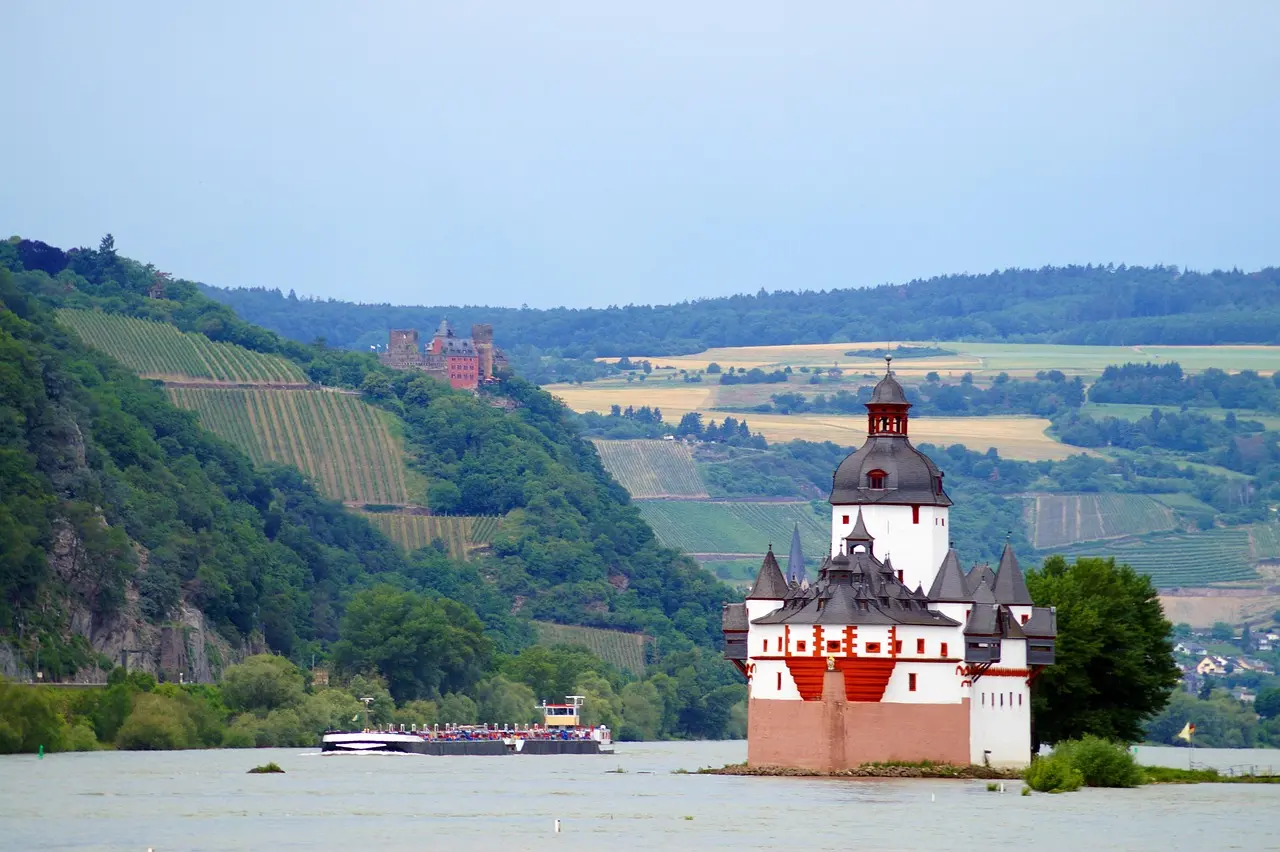 Pfalzgrafenstein Castle on its island in the Rhine, with a river boat passing and vineyards on the hills behind