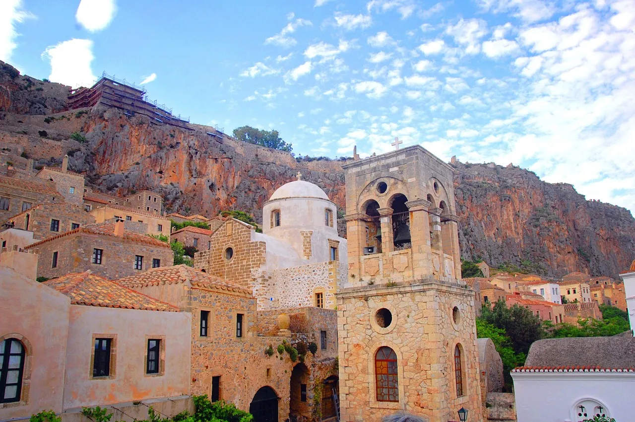 Stone houses, a domed church and a bell tower in Monemvasia's lower town, below the steep rock under a blue sky