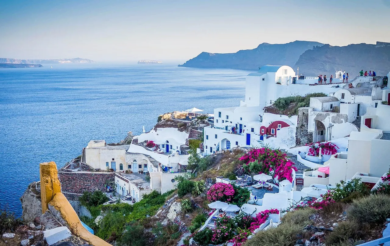White houses, blue domes and pink bougainvillea in Oia, perched on Santorini's cliffs above the sea