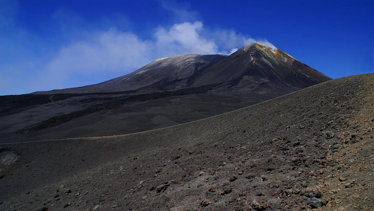 The dark, barren slopes and summit crater of Mount Etna in Sicily, with snow and clouds near the top