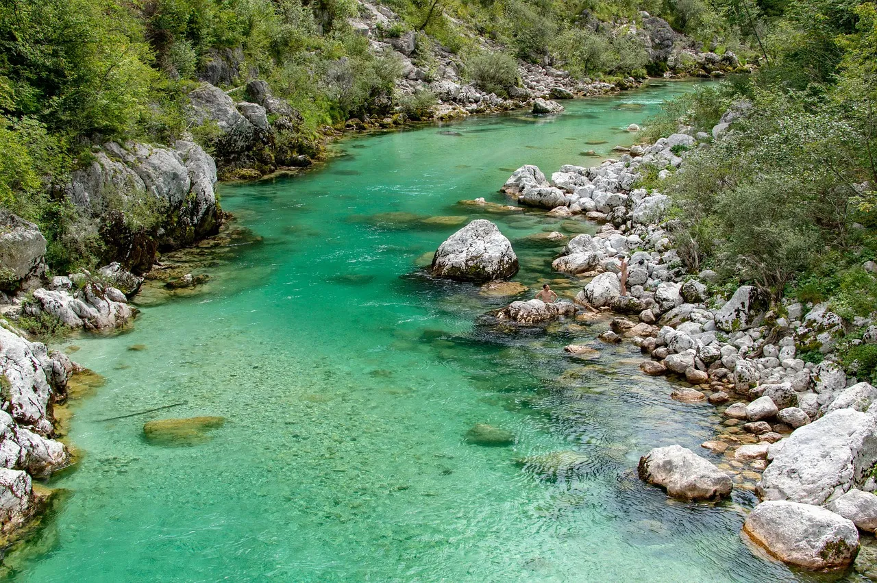 The bright turquoise water of the Soča River flowing between white limestone rocks and green forest in Slovenia