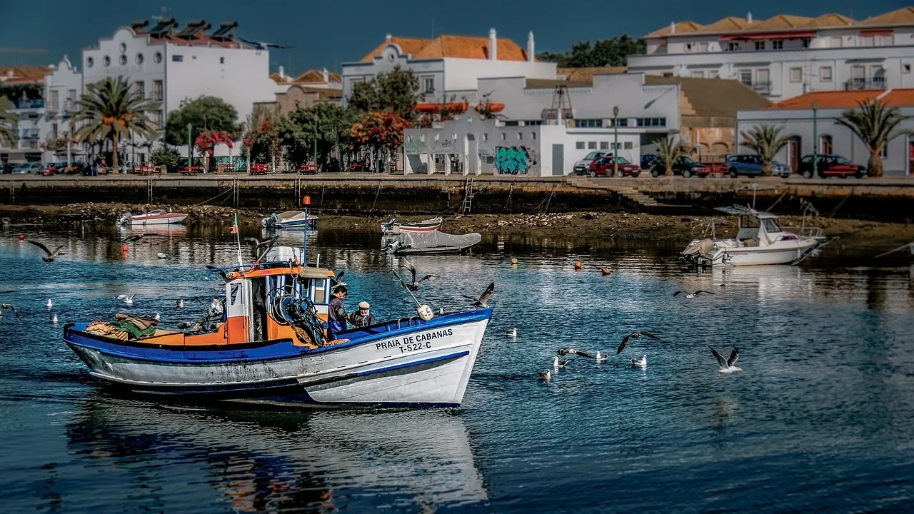 A fishing boat on the river in Tavira, with the town's white houses behind