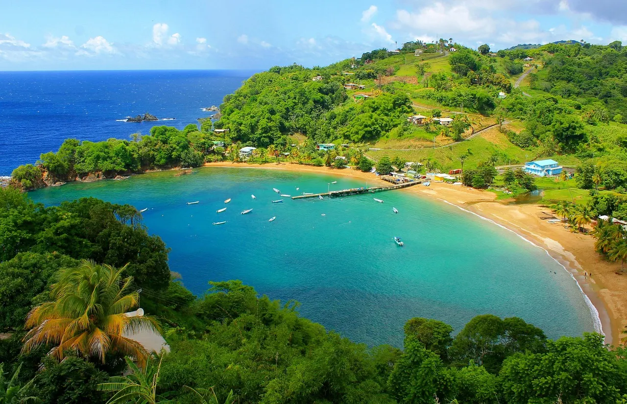 A curved sandy bay with turquoise water, small boats and green forested hills on Tobago's coast