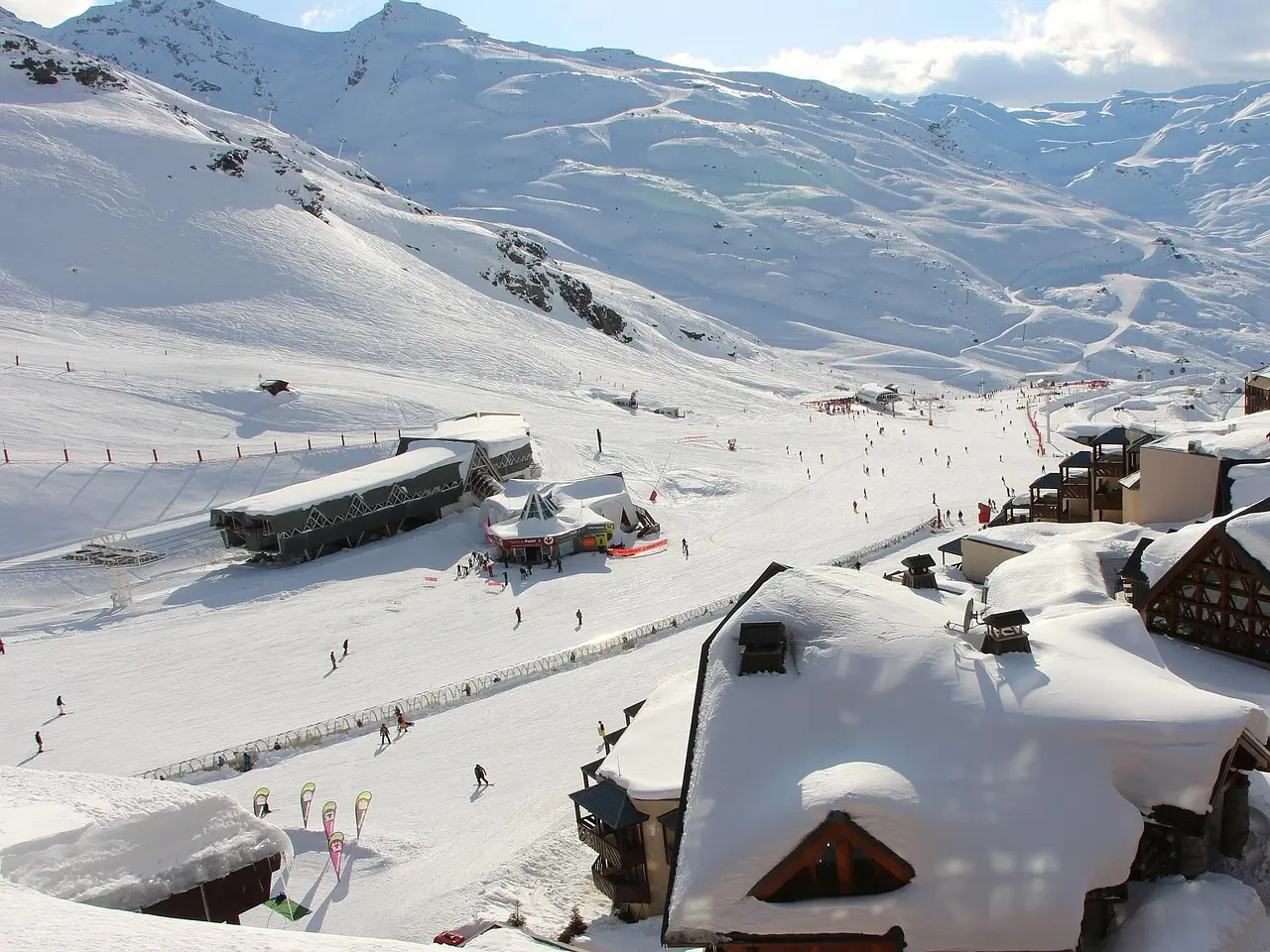 Snow-covered chalet roofs in Val Thorens looking down on busy ski slopes and lifts under white mountains