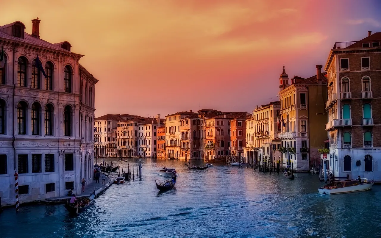 Gondolas and grand palazzi along the Grand Canal in Venice under an orange sunset sky
