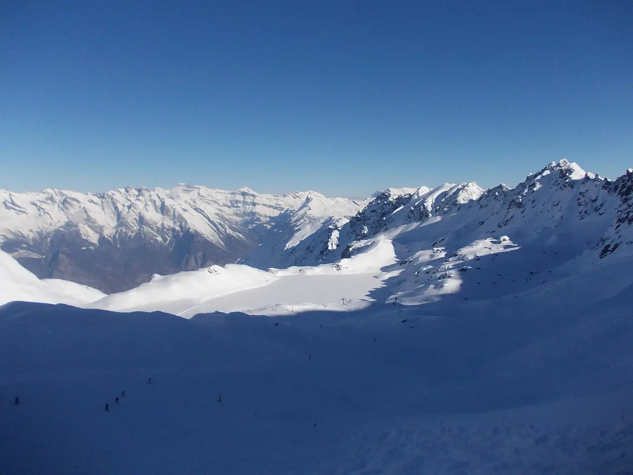 Wide snowy slopes above Verbier with a long line of snow-capped Alpine peaks under a deep blue sky