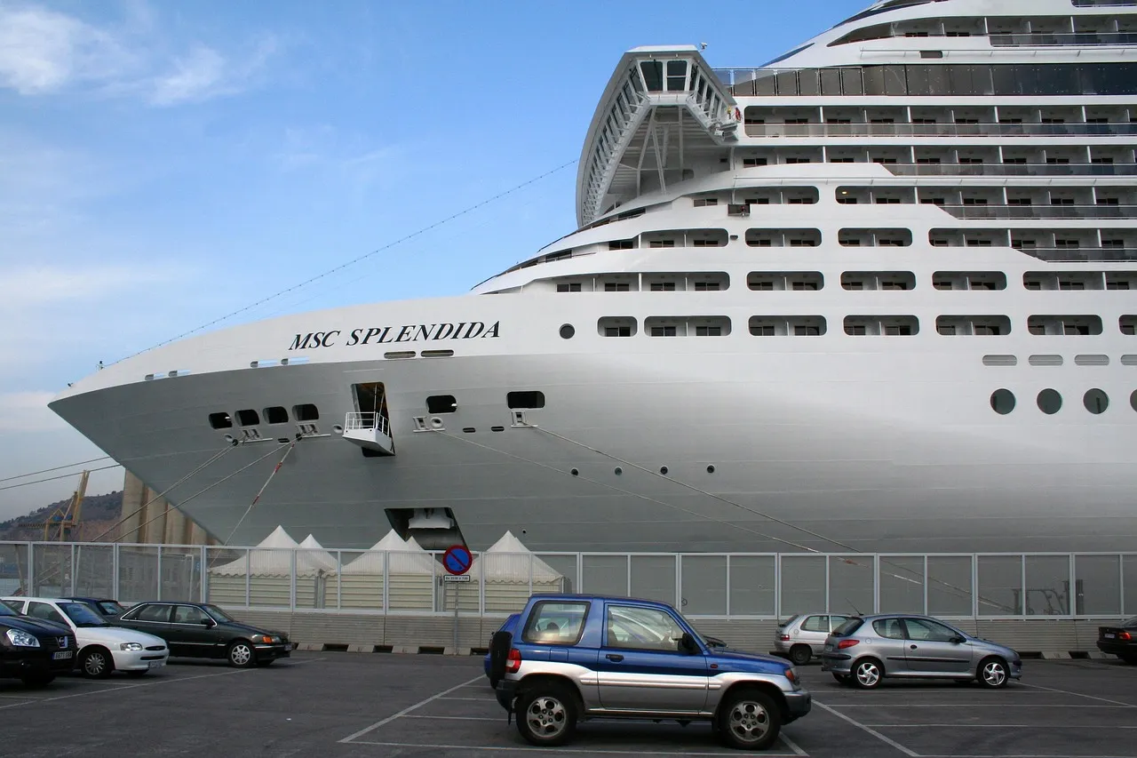 A huge white cruise ship docked at the port of Barcelona, with cars parked on the quay below