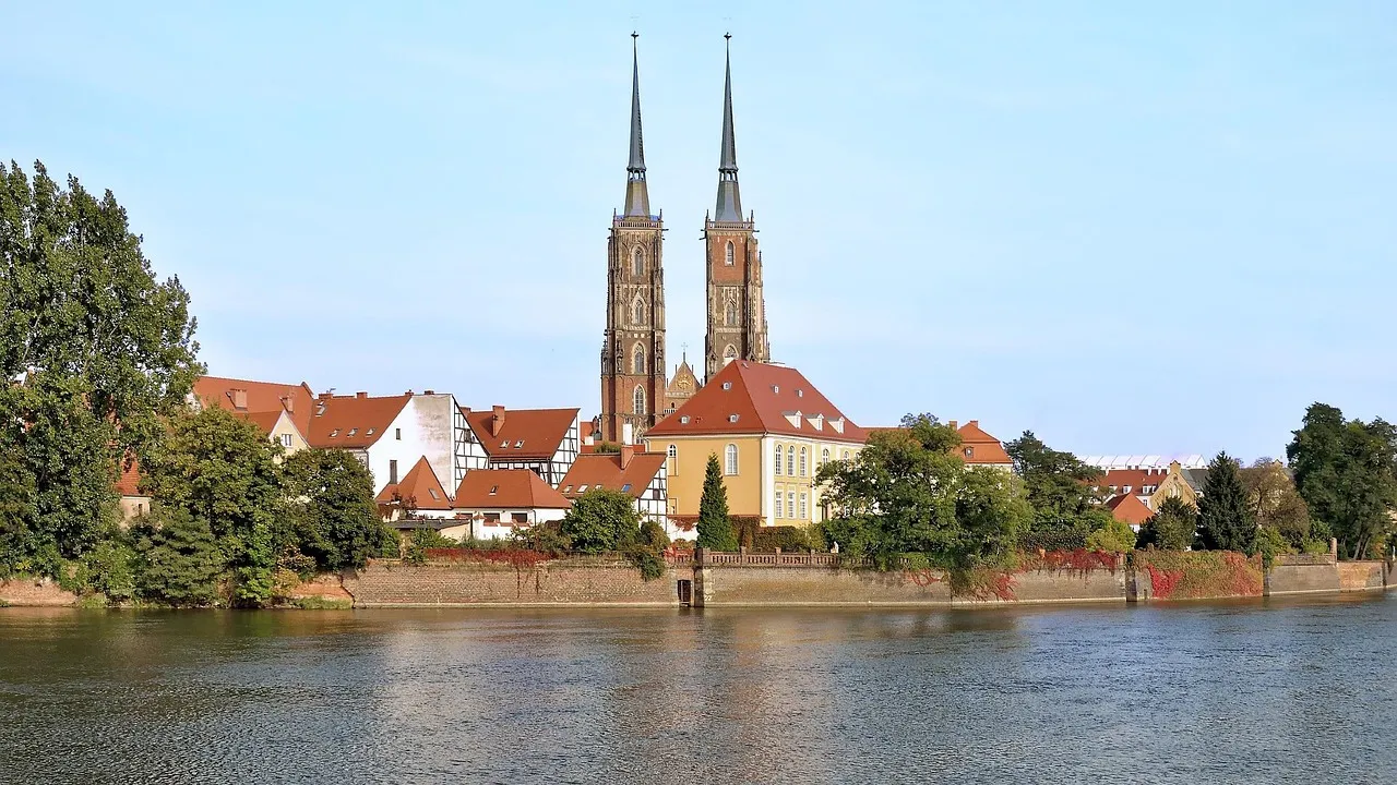 The twin spires of Wrocław Cathedral rising above red-roofed buildings on Ostrów Tumski, seen across the River Oder
